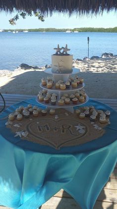 a table topped with cupcakes under a thatched umbrella next to the ocean