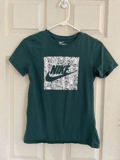 a green nike t - shirt hanging on a white door with a black and white print