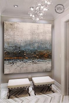 a large painting hanging on the wall above two stools in front of a chandelier