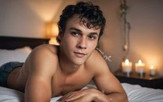 a shirtless young man laying on top of a bed with candles in the background