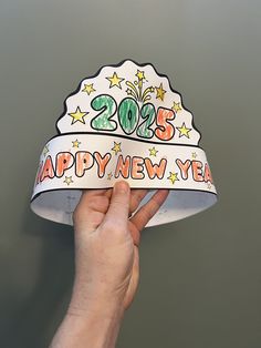 a hand holding up a paper hat with the words happy new year on it