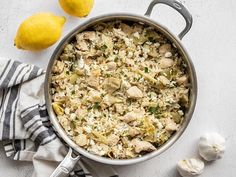 one pot lemon artichoke chicken and rice in a pan with two lemons on the side