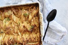 a casserole dish with potatoes and parmesan cheese on top, next to a spoon