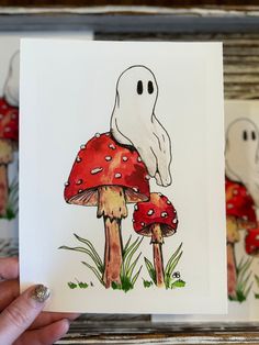 a hand holding up a card with an image of a ghost and mushrooms on it