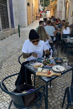 a woman sitting at a table with food in front of her on an alleyway