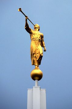 a golden statue holding a staff on top of a building with a blue sky in the background