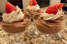 three desserts with strawberries and whipped cream in small glasses on a marble counter