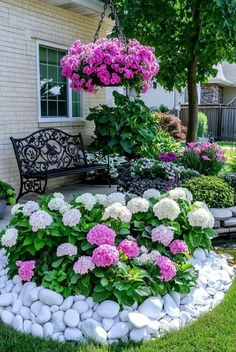 a garden filled with lots of flowers next to a bench and some rocks on the ground