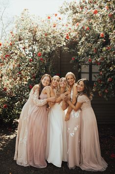 four bridesmaids pose for a photo in front of some roses at their wedding