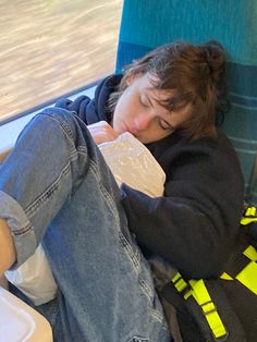 a person sleeping on a train seat with their head resting on a bag and drinking from a water bottle