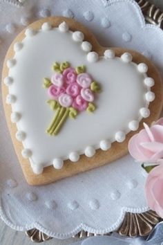 a heart shaped cookie decorated with flowers on a white doily next to pink roses