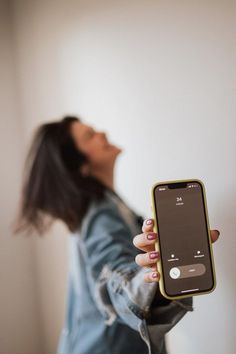 a woman holding an iphone in her hand and looking up at the sky with eyes closed