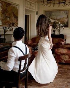 a woman in a white dress standing next to a man sitting at a dining room table