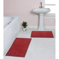 two red rugs in front of a white sink and bathtub next to a potted plant