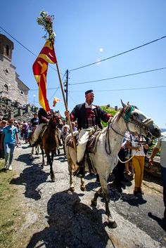 a man riding on the back of a white horse down a street next to other people