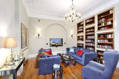 a living room filled with blue couches and chairs next to a book shelf full of books