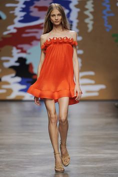 a woman in an orange dress walks down the runway