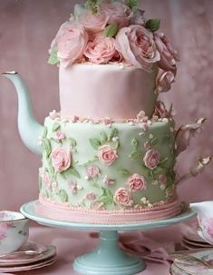 a pink and green teapot cake with flowers on the top is sitting on a table