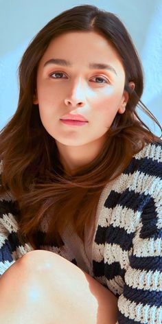 a woman with long brown hair sitting on top of a blue and white couch wearing a sweater