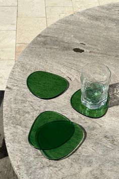 three green coasters sitting on top of a wooden table next to a glass cup