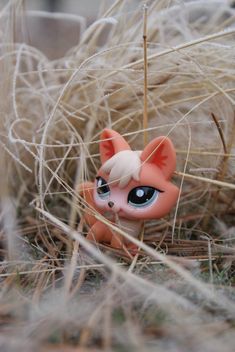 a small toy cat sitting in the grass next to some tall dry grass and weeds