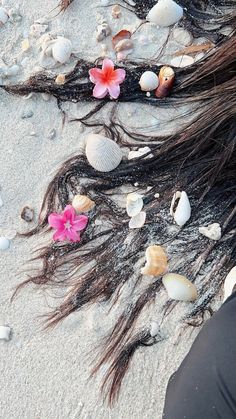 a woman laying in the sand with her hair blown back and flowers on top of it