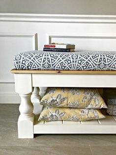 a white bench with blue and yellow pillows on it next to a book shelf filled with books