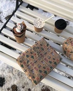 two wrapped presents sitting on top of a white bench next to cups of coffee and marshmallows