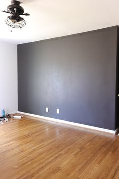 an empty room with hard wood flooring and dark gray paint on the far wall