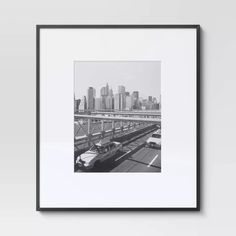 a black and white photo of a city with cars on the road in front of it