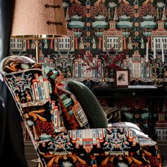 a chair and lamp in front of a wallpapered room with colorful designs on it