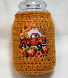 an orange crocheted jar with a red truck and pumpkins painted on it