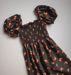 a black dress with orange flowers and ruffles on the shoulders is laying on a white surface