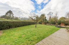 an empty backyard with a wooden deck and green grass in the foreground, surrounded by hedges