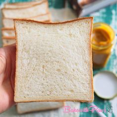 a person holding a piece of bread with peanut butter and jelly in the back ground