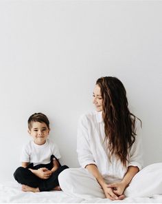 a woman sitting on top of a bed next to a little boy