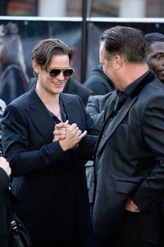 two men in suits and sunglasses standing next to each other with their hands clasped together