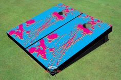 a blue cornhole board with pink and red designs on the side, sitting on green grass