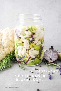 a jar filled with cauliflower and herbs next to an onion on the side