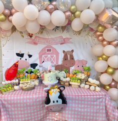 a table topped with lots of food next to white balloons and farm animals on the wall