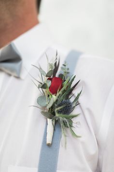 a man wearing a white shirt and blue suspenders with a boutonniere on his lapel