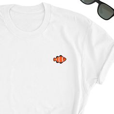 an orange clown fish on a white t - shirt next to sunglasses