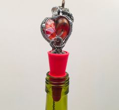 a glass bottle with a metal heart on top and a red wine stopper in the bottom