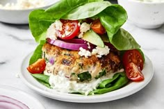 a white plate topped with meat covered in lettuce and tomatoes