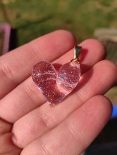 a small heart shaped piece of glass in someone's hand with a chain attached to it