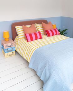 a bed with blue and yellow bedspread next to a lamp on the floor