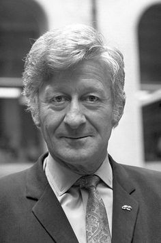 a black and white photo of a man in a suit smiling at the camera,