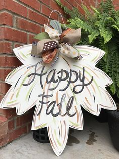 a sign that says happy fall hanging from the side of a brick wall next to a potted plant