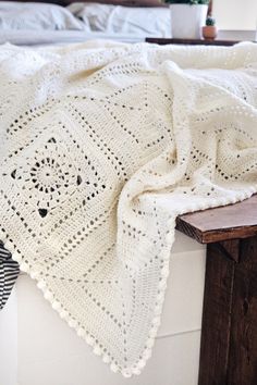 a white crocheted blanket sitting on top of a wooden table next to a bed