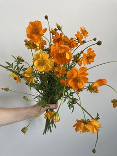 a person holding a vase filled with yellow and orange flowers on top of a table